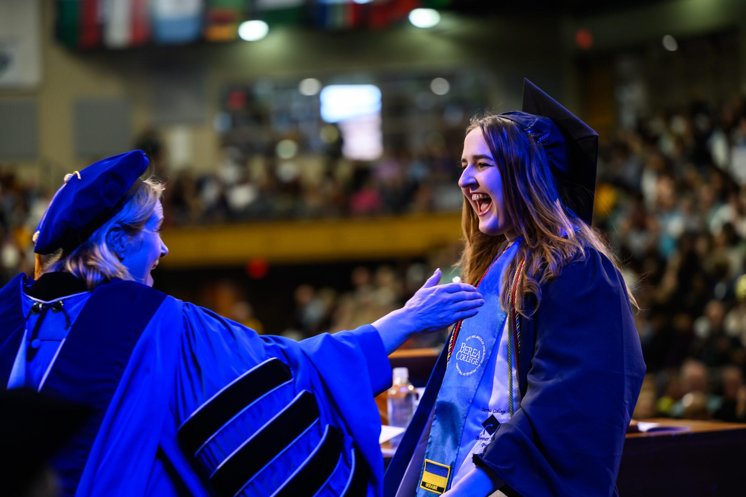 Berea College's President, Cheryl Nixon, reaching out to an excited student, as they walk across the stage at their graduation.